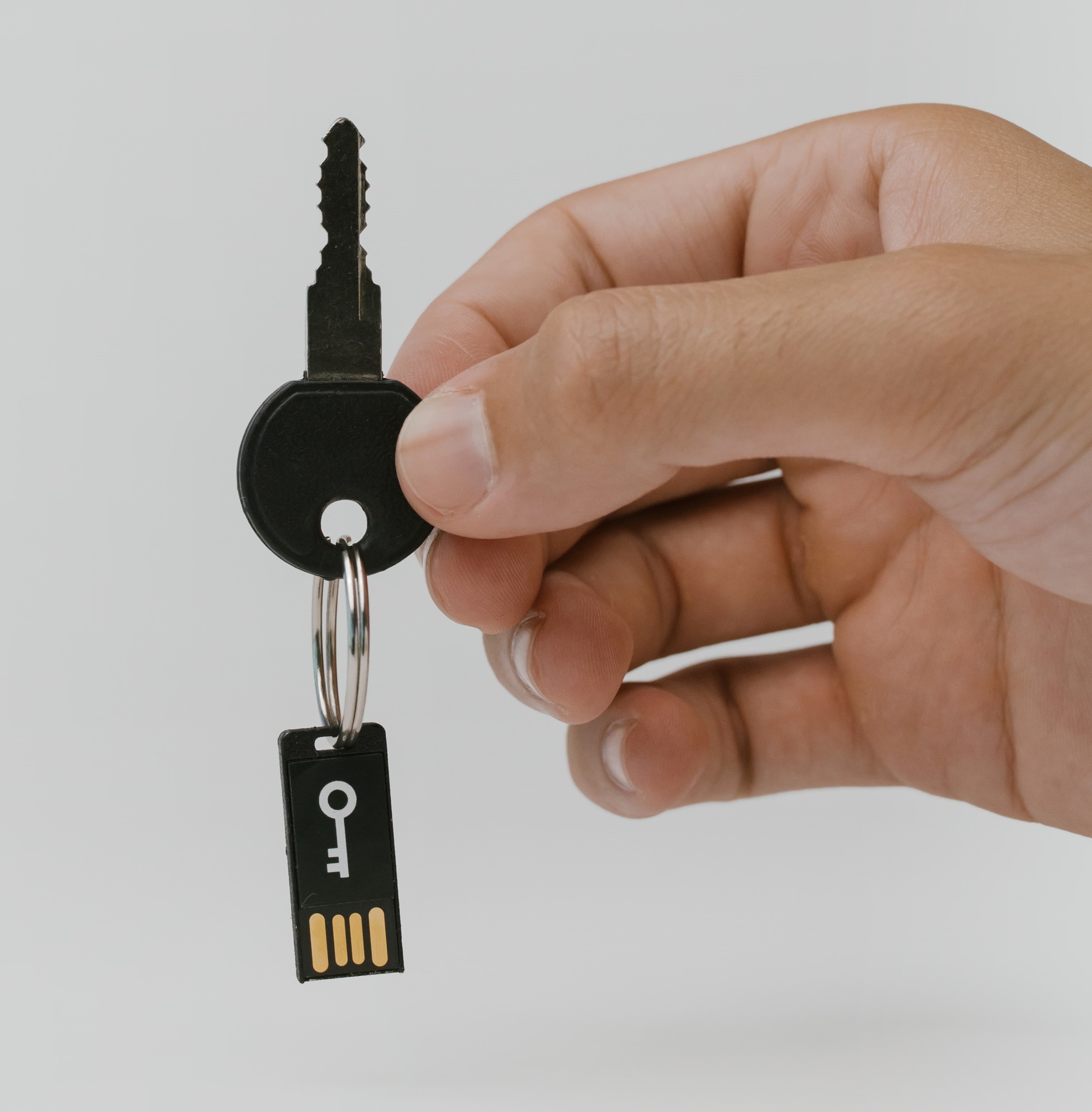 A hand holding an actual key with a key ring attached to a 2 f a device